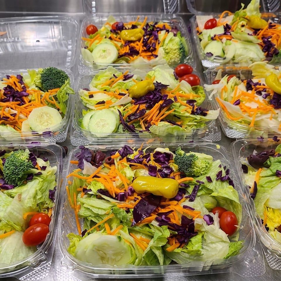 Multiple clear containers filled with fresh garden salads, including lettuce, carrots, cabbage, cucumbers, broccoli, tomatoes, olives, and peppers.